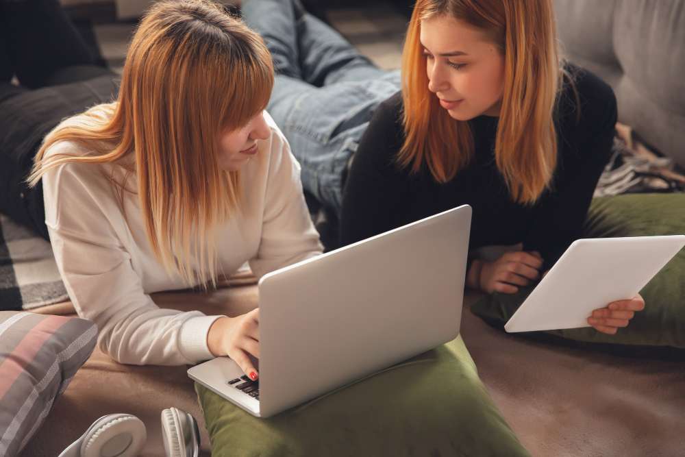 2 female talking, one of them holding a laptop